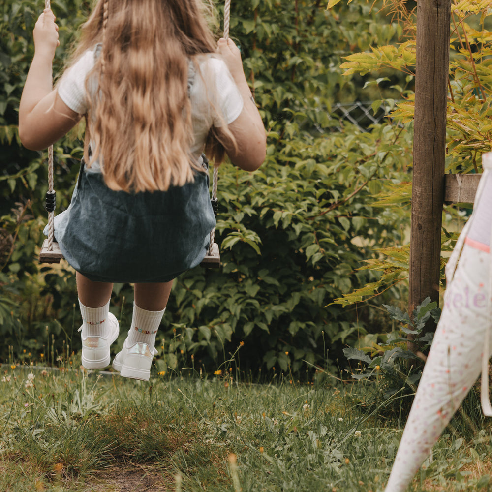 Kind auf Schaukel im Garten mit weißen „Schulkind“ Socken und Sneakern