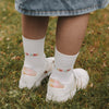 Nahaufnahme Socken „Schulkind“ mit buntem Schriftzug und weißen Sneakern im Gras