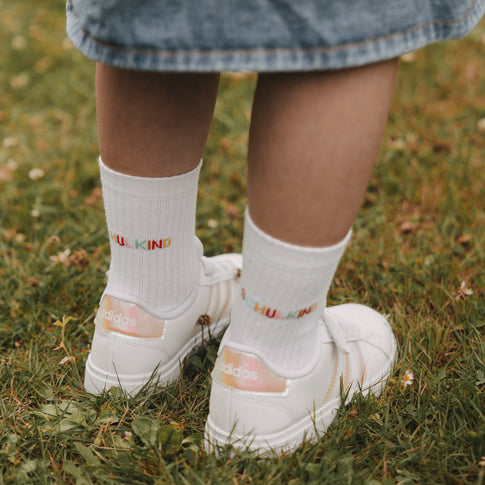 Nahaufnahme Socken „Schulkind“ mit buntem Schriftzug und weißen Sneakern im Gras