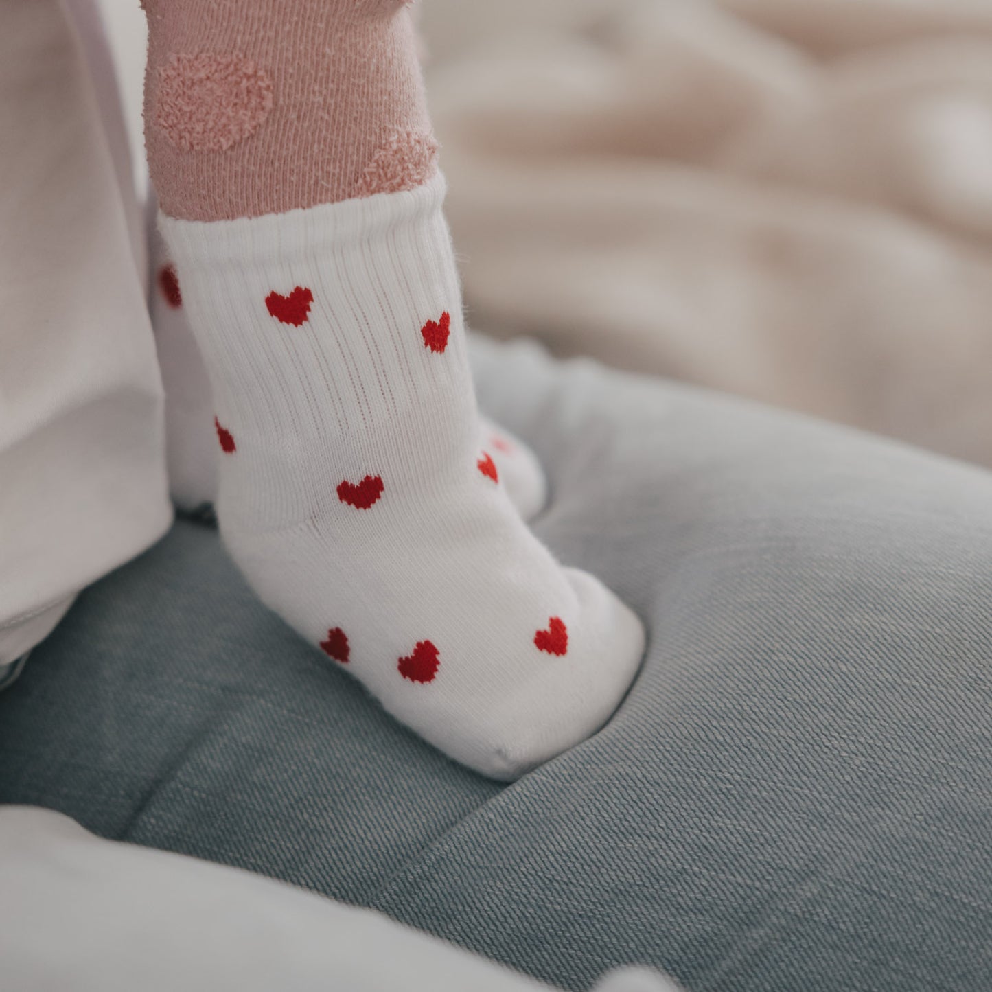 Baby trägt weiße Socken mit roten Herzen, Detailaufnahme auf Sofa, weiches Material und niedliches Design