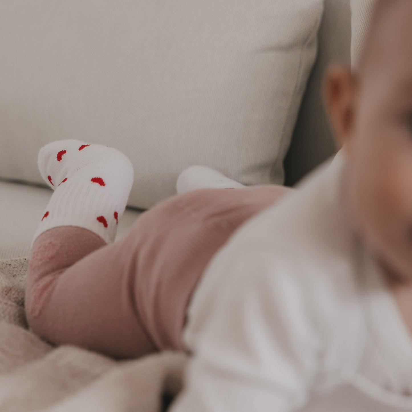Baby liegt auf Sofa mit weißen Herzsocken, gemütliche Szene mit weicher Kleidung