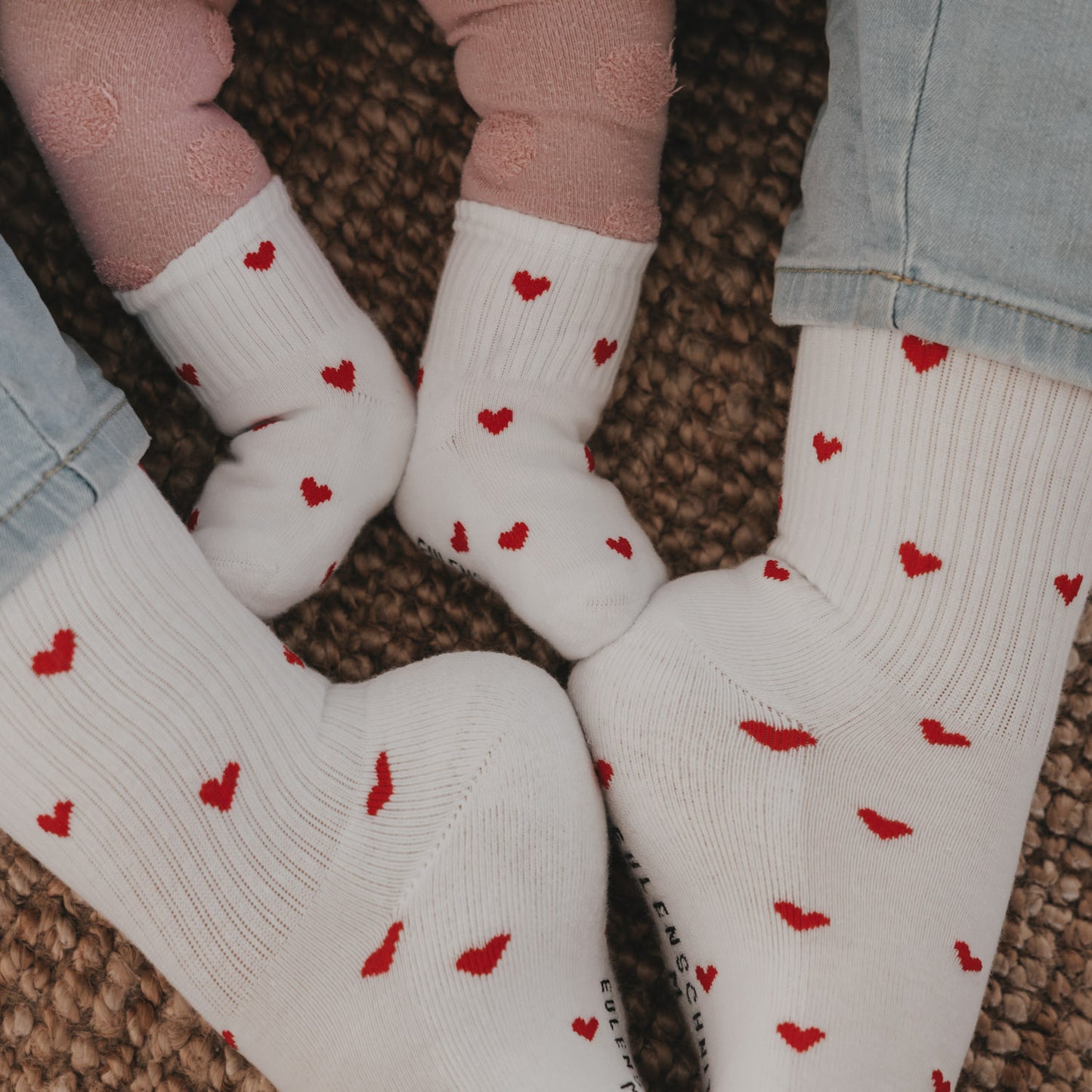 Detailaufnahme Familie mit weißen Herzsocken, liebevolles Matching-Set auf Teppich