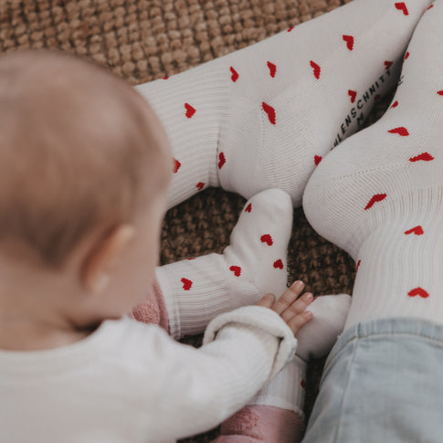 Baby und Eltern mit weißen Socken und roten Herzen, harmonische Familienszene in warmem Licht