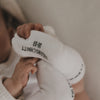 Baby greift nach Fuß, trägt weiße Socken mit Schrift „Kleines Wunder“, Nahaufnahme