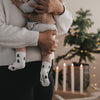 Baby mit Tannen Socken auf dem Arm, weihnachtliche Szene mit Kerzen und Tannenbaum im Hintergrund
