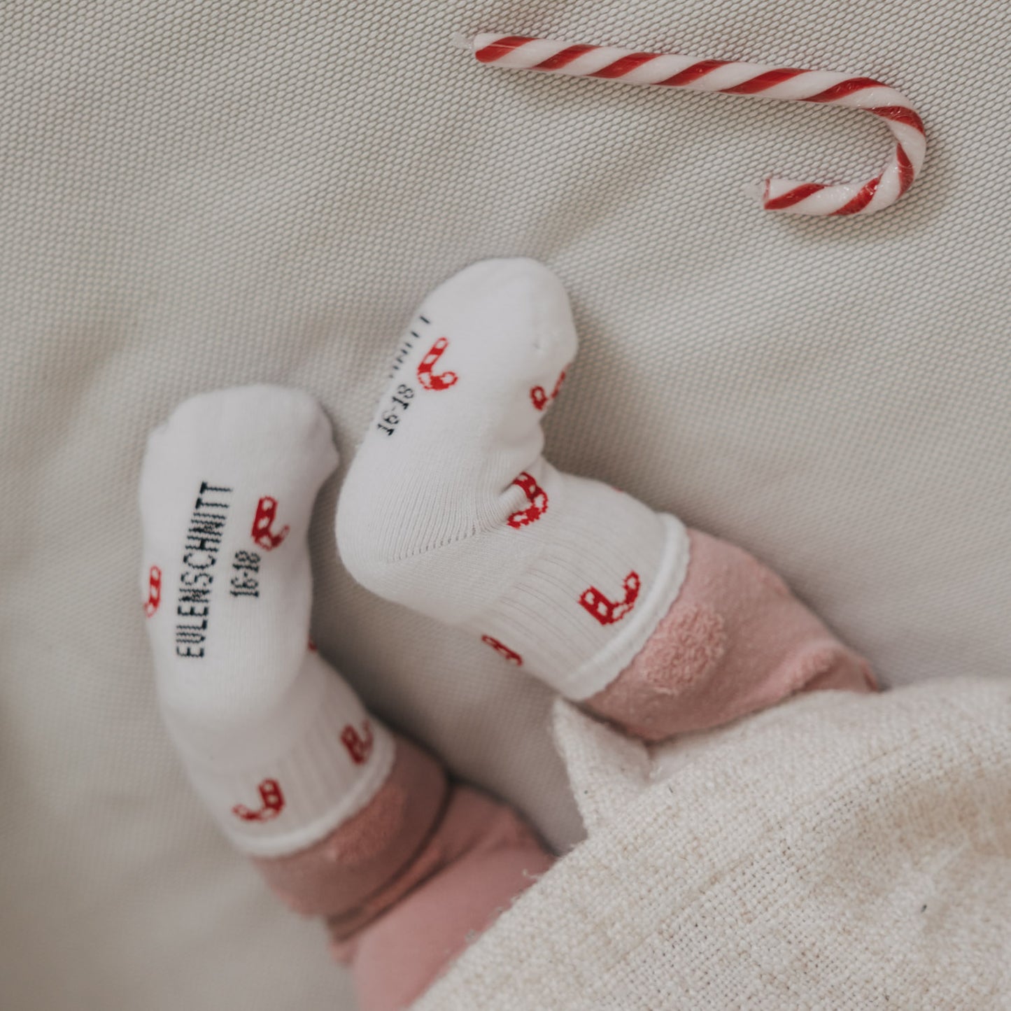 Baby liegt mit weißen Socken und Zuckerstangen Motiv, Eulenschnitt Schriftzug sichtbar