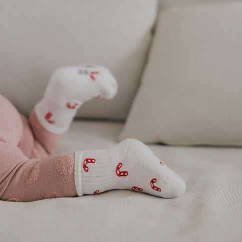 Detail Babyfuß mit weißen Socken und roten Zuckerstangen, weiches Material und gemütlicher Look