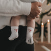 Baby wird gehalten, trägt weiße Socken mit roter Schleife, warme weihnachtliche Atmosphär
