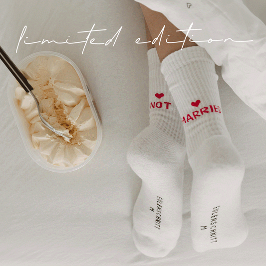 Animiertes GIF mit wechselnden Szenen: Eine Frau trägt weiße Socken mit der Aufschrift NOT MARRIED in pink und einem kleinen Herz. Sie liegt entspannt im Bett, isst Eis und bewegt dabei leicht ihre Füße. Oben im Bild steht in geschwungener Schrift Limited edition.