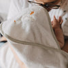 Nahaufnahme eines Babys im Arm einer Person, eingewickelt in ein weiches Kapuzenhandtuch aus Frottee. Die Kapuze mit gesticktem Gänsemotiv schützt den Kopf und sorgt für wohlige Wärme.