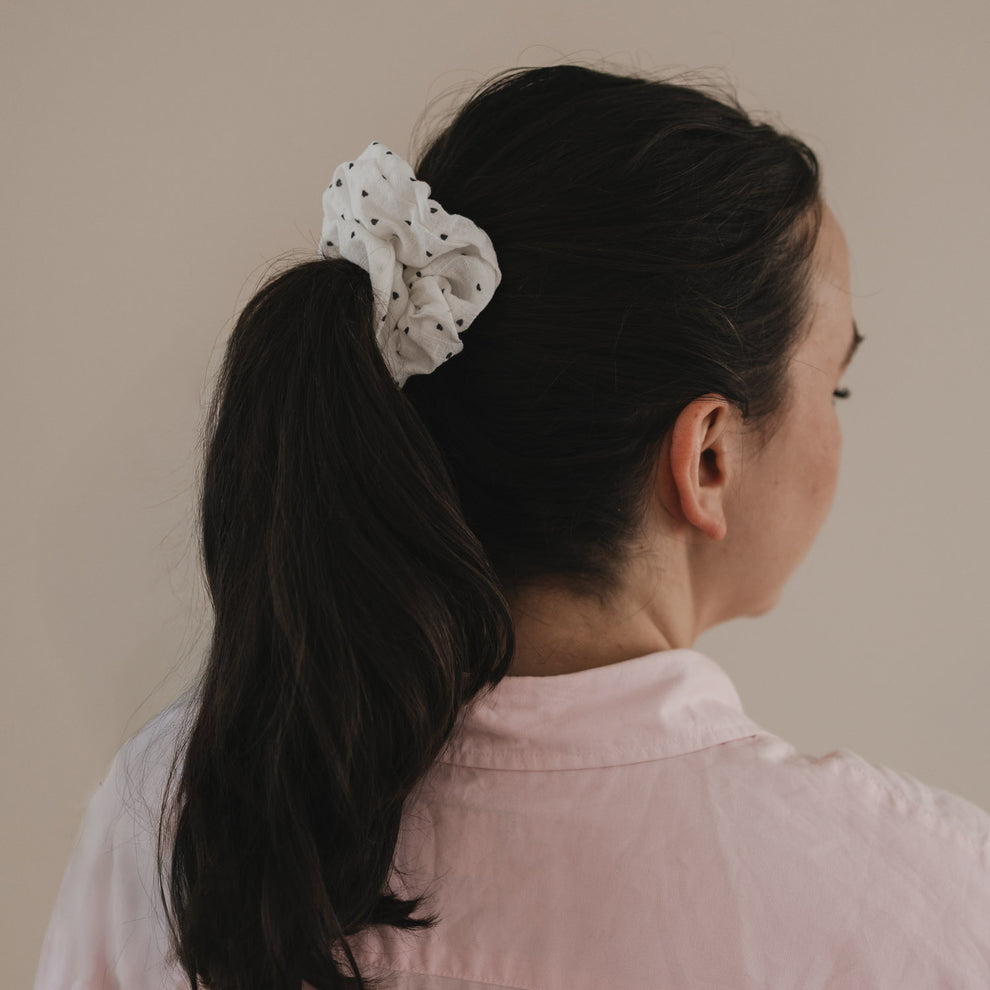 Weißes Scrunchie mit kleinen schwarzen Herzen hält Pferdeschwanz im braunen Haar