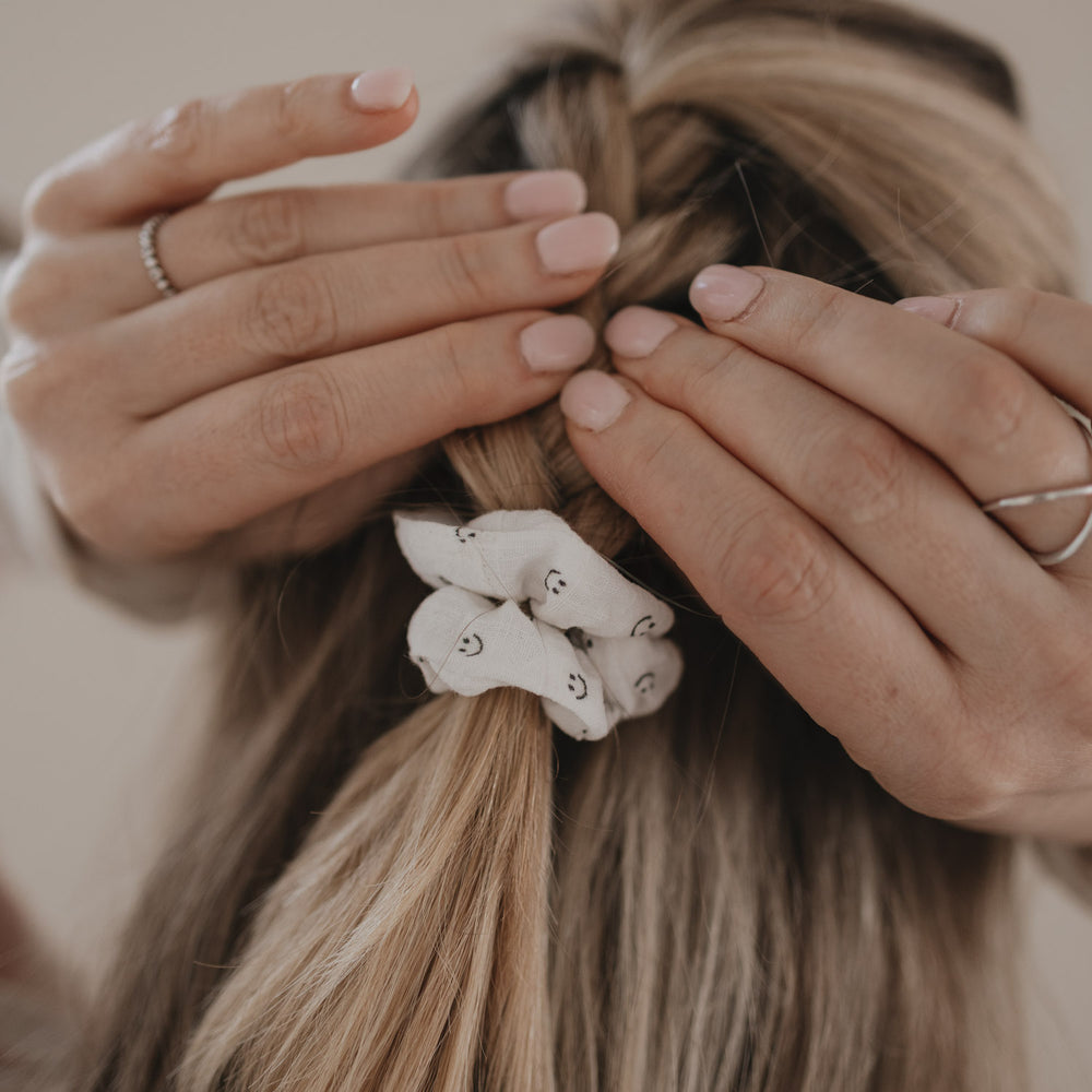 Hände befestigen Scrunchie mit Smiley-Muster im geflochtenen Haar