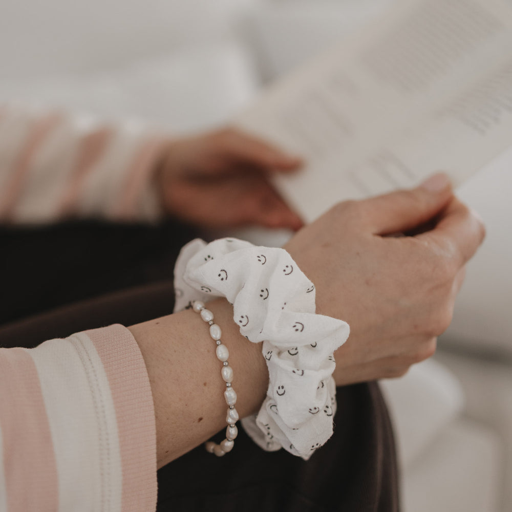 Weißes Scrunchie mit Smiley-Muster am Handgelenk getragen