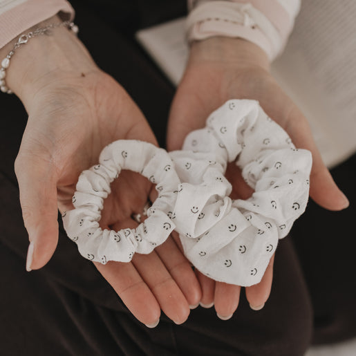 Zwei Scrunchies mit Smiley-Muster in unterschiedlichen Größen in den Händen präsentiert