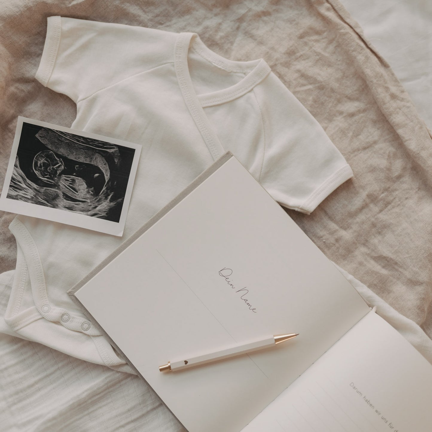 Schwangerschaftstagebuch offen mit Seite „Dein Name“ neben Babybody und Ultraschallfoto.