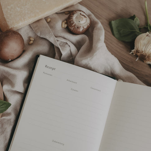 Geöffnete Rezeptseite im Rezeptbuch umgeben von Pilzen, Käse und Kräutern