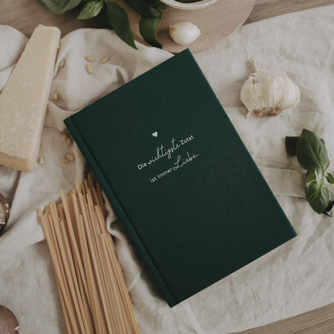 Rezeptbuch „Wichtigste Zutat“ auf Küchentuch umgeben von Pasta und frischen Zutaten