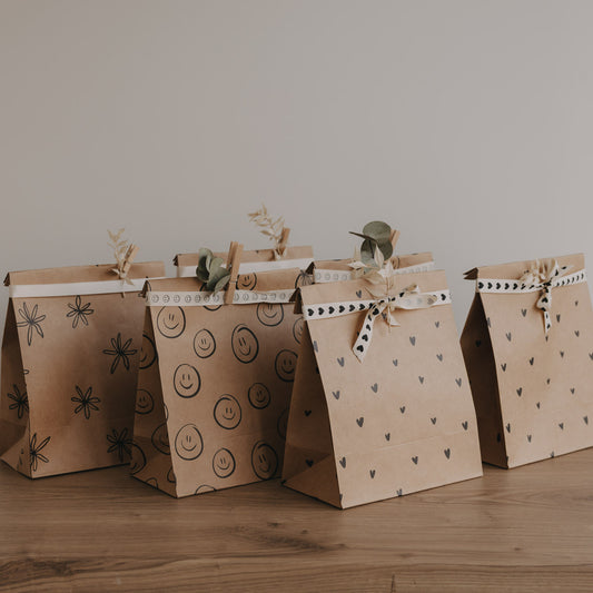 Papier Geschenktüten mit Herz-, Smiley- und Blumenmotiven im Set, dekorativ aufgereiht auf Holztisch