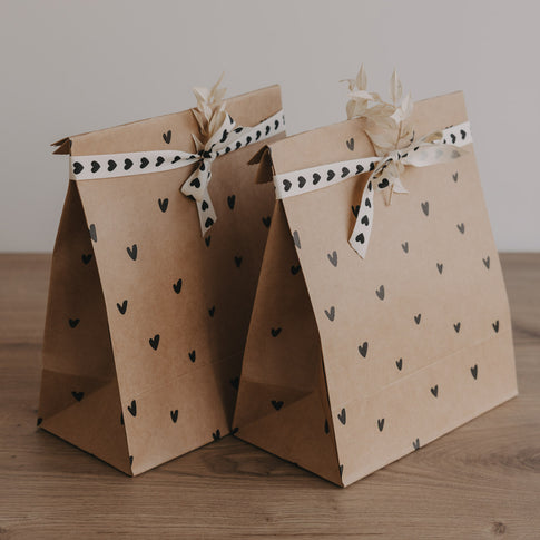 Papier Geschenktüte mit Herzmuster, Schleife und Trockenblume wird von Hand gehalten