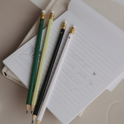 Vier Bleistifte in Grün, Weiß, Schwarz und Hellgrün auf Notizblock