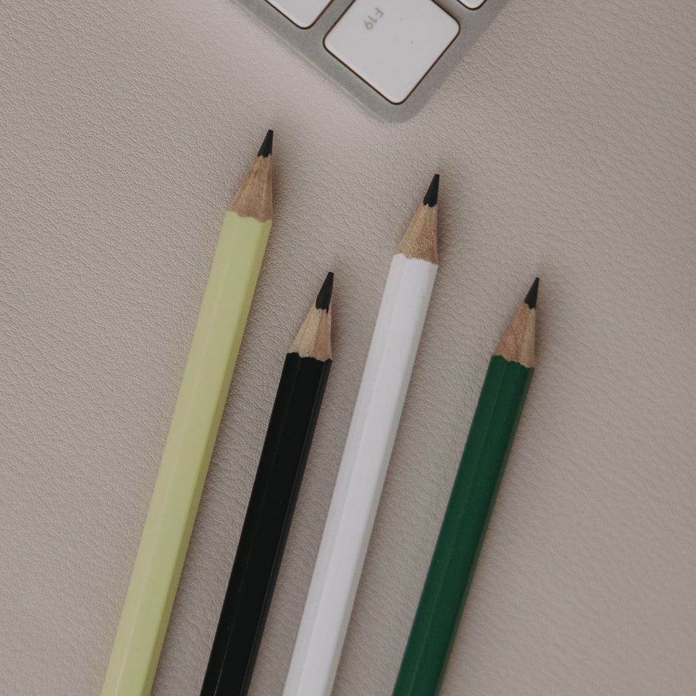 Vier angespitzte Bleistifte in Grün, Weiß, Schwarz und Hellgrün auf Schreibtisch