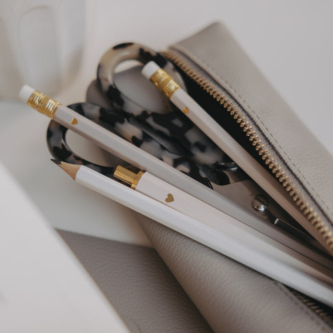 Cremefarbene und weiße Bleistifte mit goldenen Details neben Schere und Etui