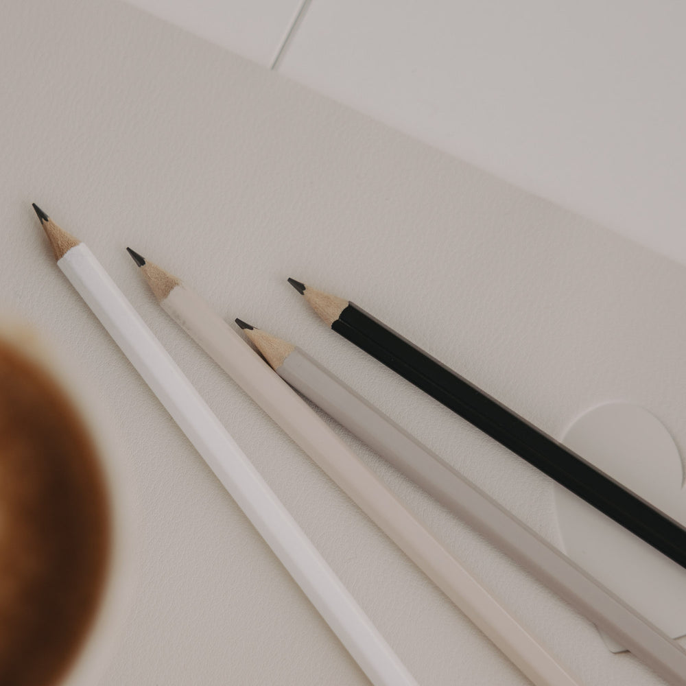 Vier angespitzte Bleistifte in Creme, Weiß und Schwarz auf hellem Untergrund