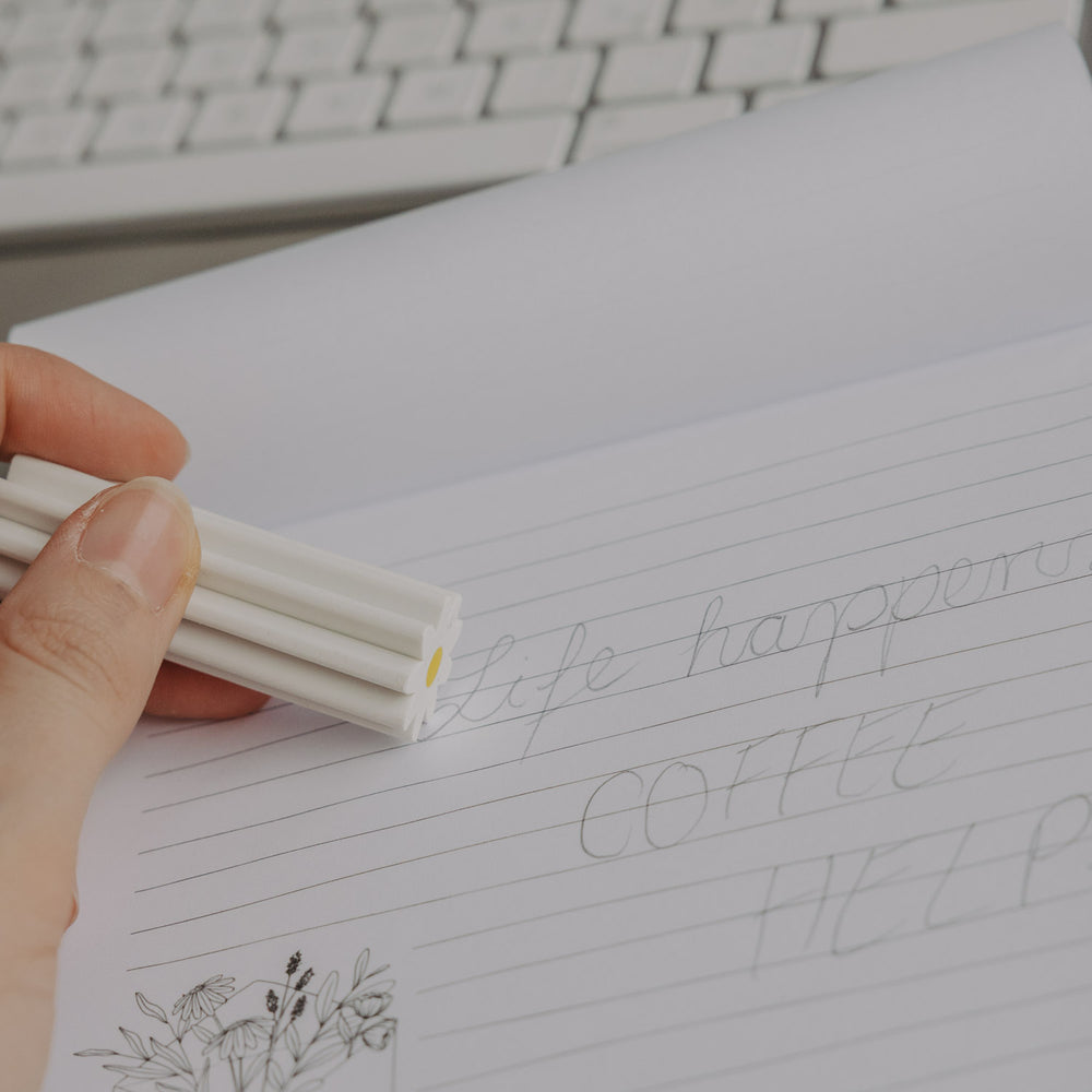 Hand hält Radiergummi Daisy und radiert auf linierten Notizblock