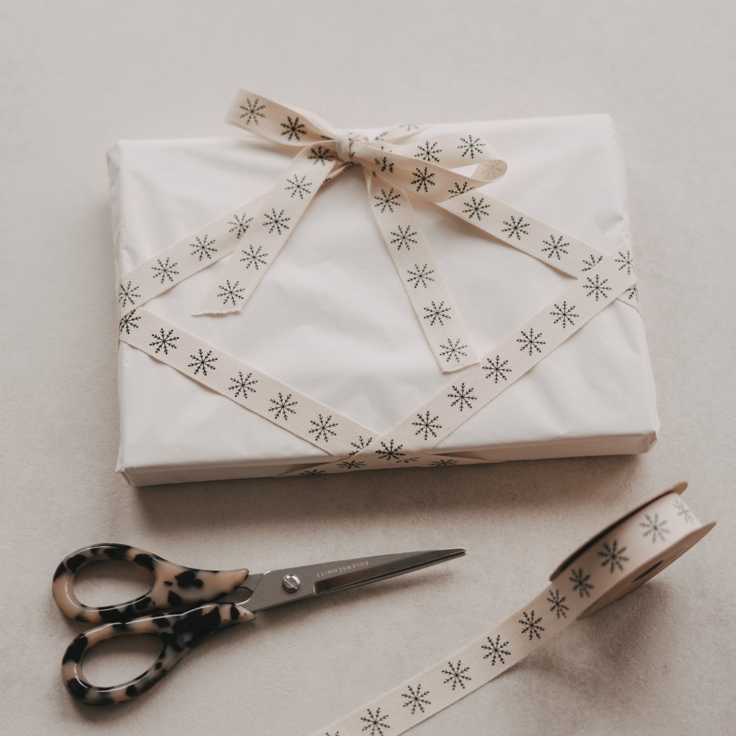 Weißes Weihnachtsgeschenk mit beigem Eulenschnitt Geschenkband und schwarzen Schneeflocken