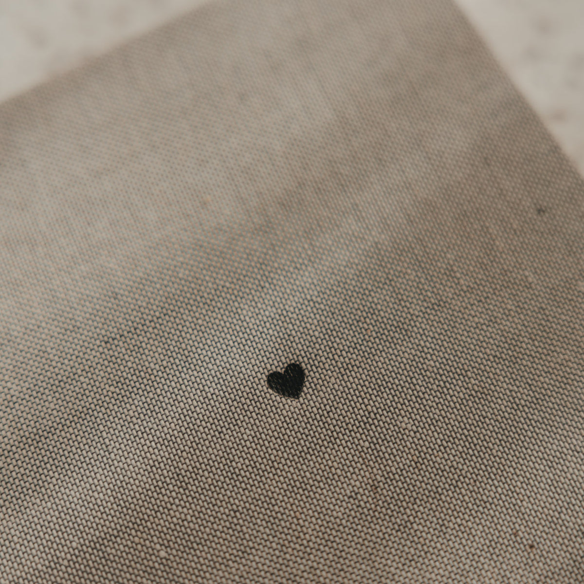 Detail des grau beigen Stoffeinbands vom karierten A5 Notizbuch mit kleinem schwarzem Herz
