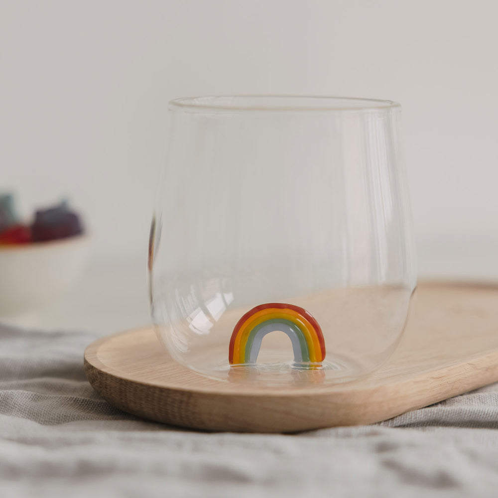Glas mit buntem Regenbogen am Boden, modernes Trinkglas auf Holztablett